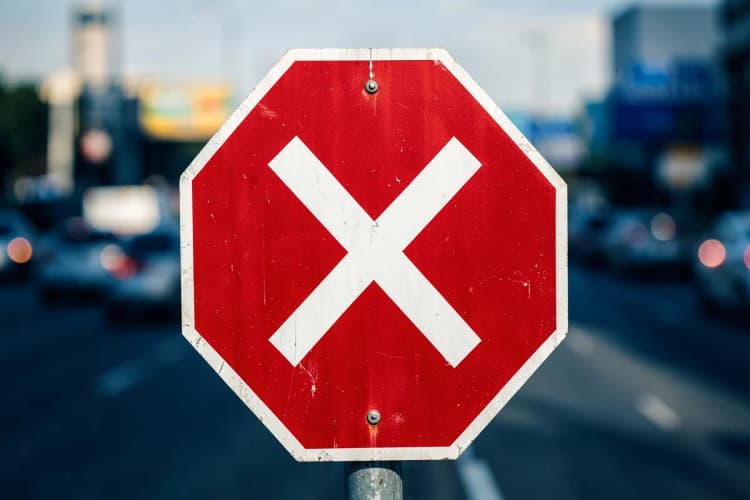 Um sinal de "pare" vermelho com um "X" branco sobre ele, em um fundo desfocado de tráfego.