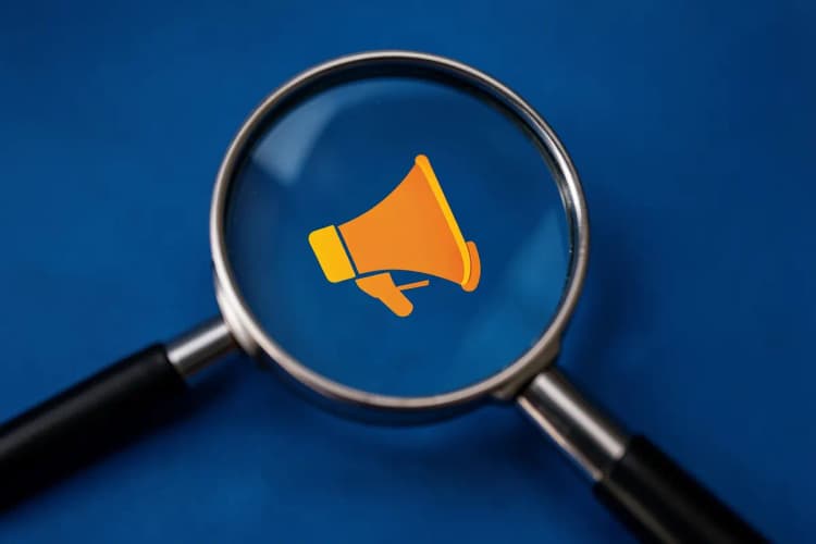 Uma lupa focando em um ícone de megafone em um fundo azul, representando a promoção de um e-commerce.