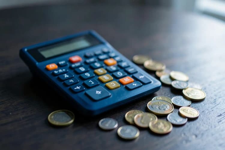 Uma calculadora e moedas de dinheiro sobre uma mesa de madeira escura.